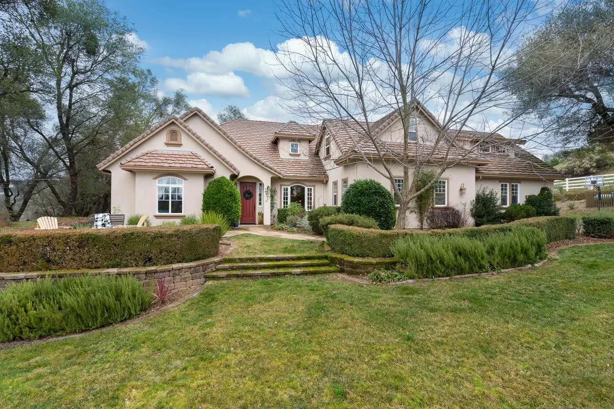 A suburban house with a landscaped front yard, featuring hedges and a pathway, set against a backdrop of trees and a partly cloudy sky.
